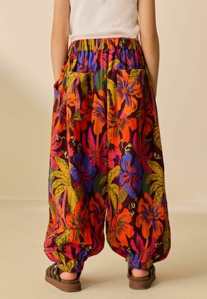Person wears loose, high-waisted pants with elastic cuffs and vibrant tropical floral print in orange, purple, green, and pink.