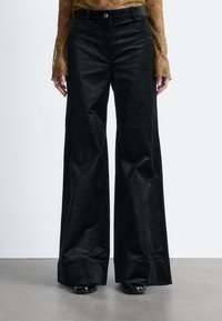 Schwarze Cord-weitbeinige Hose mit strukturiertem Finish, ausgestattet mit einem vorderen Knopfverschluss und seitlichen Taschen. Die Hose hat eine taillierte Passform.