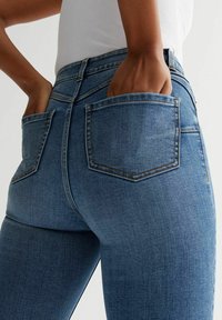 Dark blue denim jeans featuring back pockets, a fitted design, and visible stitching details at the waistband and pocket edges.
