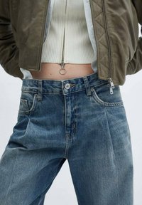 Jeans de mezclilla azul de corte medio, con una textura desgastada, que presentan un corte recto, cinco bolsillos y un cierre de botón.