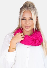 Écharpe infinity fuchsia en tissu texturé, tombant de manière décontractée autour du cou, associée à une chemise blanche à boutons.