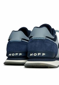 Een paar blauw en grijze sneakers met "HOFF" gedrukt op de hiel, getoond vanuit de achterkant op een witte achtergrond.