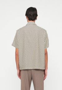 Korte mouwen shirt in beige met een geometrisch zwart-wit patroon, met een kraag en een relaxte pasvorm.