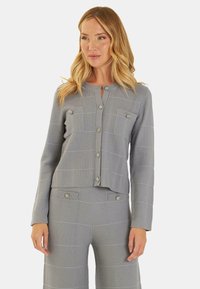 Cardigan grigio in maglia con texture, caratterizzato da un collo rotondo, tasche frontali e dettagli in bottoni metallici. Abbinato a pantaloni coordinati.