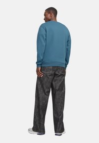 Sweatshirt bleu à col rond et poignets côtelés, associé à un pantalon sombre à texture lâche et des baskets blanches.