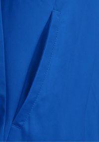 Tela azul con una superficie texturizada, que presenta un bolsillo lateral y una costura precisa. El material parece duradero y suave.