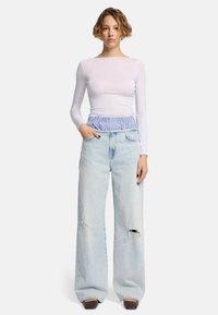 Weißes Langarmoberteil mit enganliegendem Schnitt und blauer gestreifter Taille, kombiniert mit hellblauen hochtaillierten, weit geschnittenen Jeans mit verwaschenen Details.
