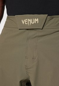 Olive green shorts made of lightweight fabric, featuring a VENUM logo on a structured waistband and flatlock seams for durability.