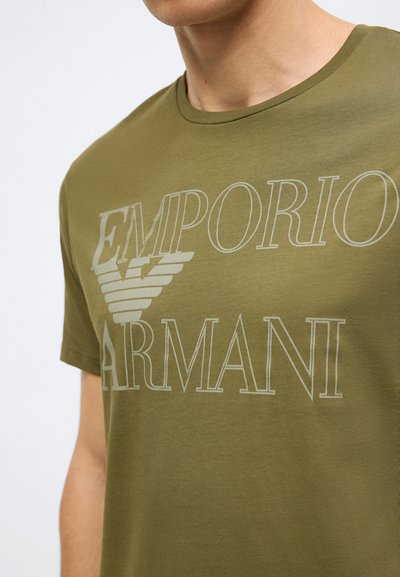 Olivzaļš kokvilnas T-krekls ar apaļu apkakli un priekškrasā logotipu ar tekstu "EMPORIO ARMANI" un spārnotu emblēmas dizainu.