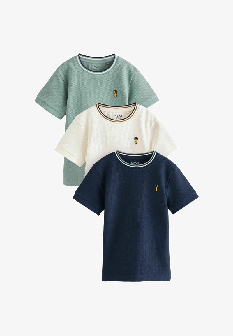 Trois t-shirts texturés à manches courtes en vert, blanc et bleu marine, chacun avec un petit homard jaune brodé sur la poitrine gauche.