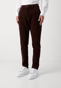 Bruna kordbry pants med rakt ben, med knappstängning och fickor, matchade med vita sneakers.