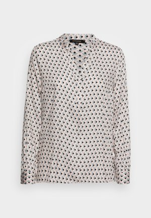 Blouse à manches longues avec un motif géométrique en losanges rose et noir et un petit col en V sur fond neutre.
