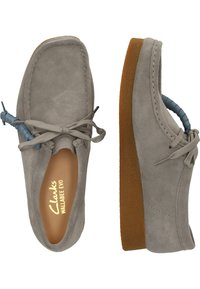 Des chaussures Clarks Wallabee Evo en daim gris avec des accents de lacets bleus. Bout rond, col rembourré, semelle en caoutchouc avec finition texturée.