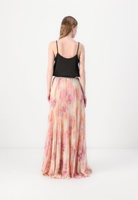 Schwarzes Spaghetti-Trägertop kombiniert mit einem langen, gefältelten Rock, der ein pastellfarbenes Blumenmuster in Rosa und Orange auf einem hellen Hintergrund hat.