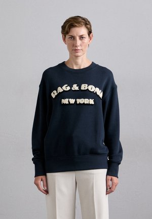 Jūras spēku treniņtērps ar teksturētu krēmkrāsas uzrakstu "RAG & BONE NEW YORK." Iespējota apaļa kakla izgriezne un ribotās piedurknes. Mīksts audums.