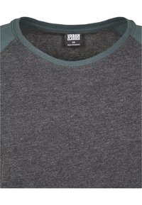Camiseta de color gris oscuro con escote redondo, con mangas raglán de un gris más oscuro, hecha de tejido suave. Etiqueta de la marca visible en el interior.