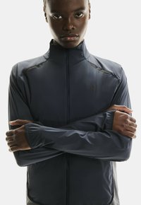 Veste légère marine avec un col haut, des manches longues et une fermeture zip ; présente un design élégant et un discret logo sur la poitrine.
