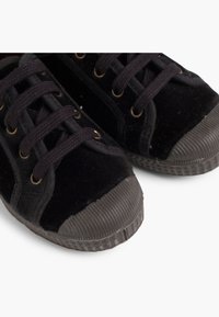 Sneakers neri in tela con lacci neri e punte e suole in gomma texturizzata su uno sfondo bianco.