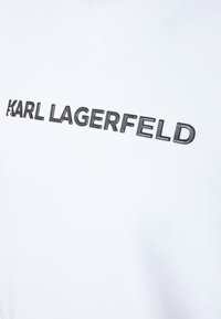 Camiseta de algodón blanca con un audaz logo negro "KARL LAGERFELD" impreso en el pecho. Tejido suave con una textura lisa.