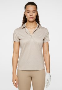 Polo beige con un design a motivi sottili, maniche corte e colletto. Presenta bottoni al collo. Accompagnato da un guanto da golf bianco.