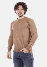 Maglione marrone lavorato a maglia con collo rotondo, maniche lunghe e polsini a coste, abbinato a jeans blu. Tessuto dalla trama liscia e di peso medio.
