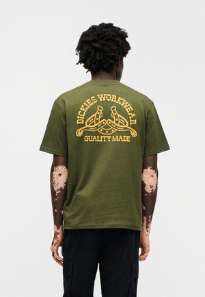 Λαδί βαμβακερό t-shirt με κίτρινο γραφικό σχέδιο στην πλάτη που γράφει "Dickies Workwear Quality Made." Κοντά μανίκια, άνετη εφαρμογή.