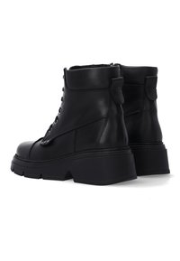 Pár černých kožených kotníkových bot na šněrování s silnými platformami a poutky vzadu, zobrazeno ze zadní strany.