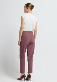 Witte mouwloze top, bordeauxrode slim-fit broek met zijzakken en donkerrode hoge hakken. Soepele stof met strakke lijnen en op maat gemaakt ontwerp.