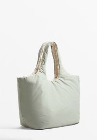 Sac fourre-tout matelassé vert clair avec une texture douce, un sommet arrondi et des doubles poignées. Il offre un design spacieux et une doublure intérieure contrastante.