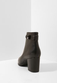 Braune Leder-Stiefeletten mit runder Zehenpartie, mittelhohem Blockabsatz und einem glänzenden Schnallenriemen-Detail am Knöchel. Glatte Textur und elegantes Design.