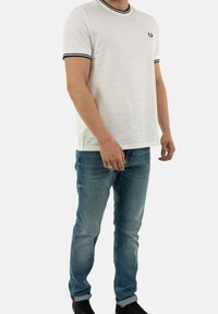 Camiseta blanca de algodón con cuello y detalles en las mangas en canalé negro, combinada con vaqueros azules de mezclilla de corte clásico y lavado claro.