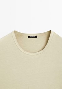 T-shirt beige in cotone con scollatura rotonda e maniche corte. Etichetta con la scritta "Massimo Dutti" e "Made in Portugal." Texture liscia.