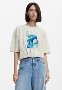 T-shirt oversize couleur crème avec un graphique de fruits bleus, fabriqué en coton doux. Associé à un jean en denim bleu clair taille haute.