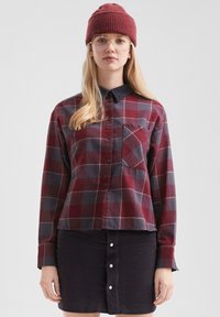 Rood en marineblauw geruite overhemd met lange mouwen en een borstzak, gecombineerd met een marineblauwe corduroy rok met knoopdetails.