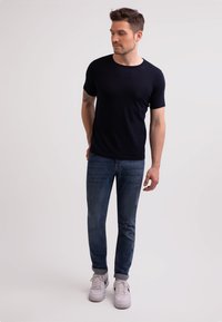Mörkblå kortärmad t-shirt i mjuk bomull, kombinerad med slim-fit mörka jeans och grå sneakers, med en rund halsringning och diskret sömnad.