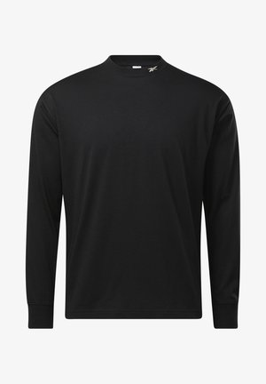 Mustapaita pitkällä hihalla ja pyöreällä kaula-aukolla, yhdistettynä mustiin verkkareihin. Vaatteet täydentää vaaleat lenkkarit, joissa on teksturoitu pohja.