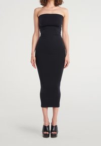 Abito midi nero senza spalline realizzato in tessuto elasticizzato. Silhouette aderente con una trama liscia. Paio di scarpe con plateau nere con cinghie incrociate.