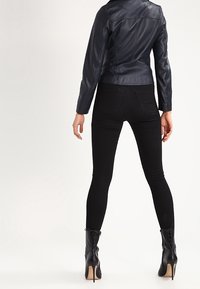 Černá kožená bunda s přiléhavým střihem, kombinovaná s černými slim kalhotami a černými vysokými botami na podpatku, viděná zezadu.