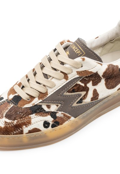 Sneaker a stampa mucca marrone e beige con lacci crema, dettagli grigi e suola trasparente. Presenta un logo sulla linguetta e una tomaia testurizzata.
