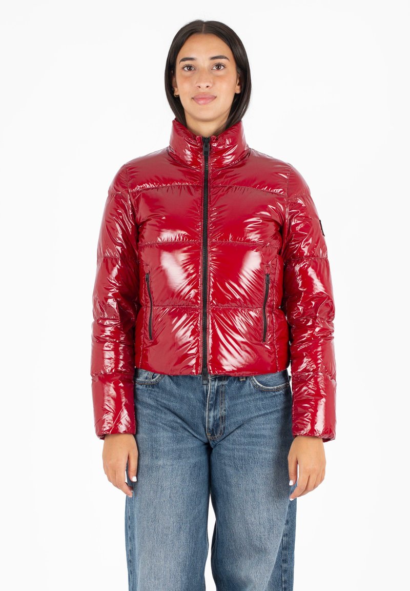 Rode glanzende pufferjack met hoge kraag, ritssluiting aan de voorkant en twee zijzakken. Gedragen over blauwe denim, met een cropped ontwerp.