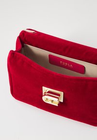 Borsa a pochette in velluto rosso con hardware dorato, caratterizzata da una forma rettangolare, chiusura con zip e una foderatura interna beige con etichetta logo.