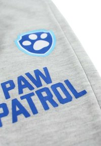 Tissu gris avec texte "PAW PATROL" en bleu et un bouclier bleu clair avec un emblème d'empreinte de patte. Texture douce et lisse.