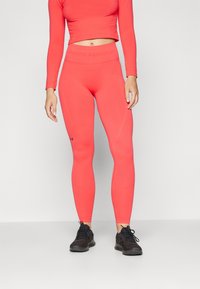 Lys korallfarget langermet topp med kort skjæring, kombinert med matchende høy midje leggings. Slank passform, elastisk stoff og logo på midjen. Sorte treningssko.