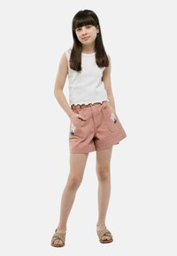 Un short rose clair avec une broderie florale sur les poches, associé à un débardeur blanc à côtes avec un ourlet festonné. Porté avec des sandales tressées.