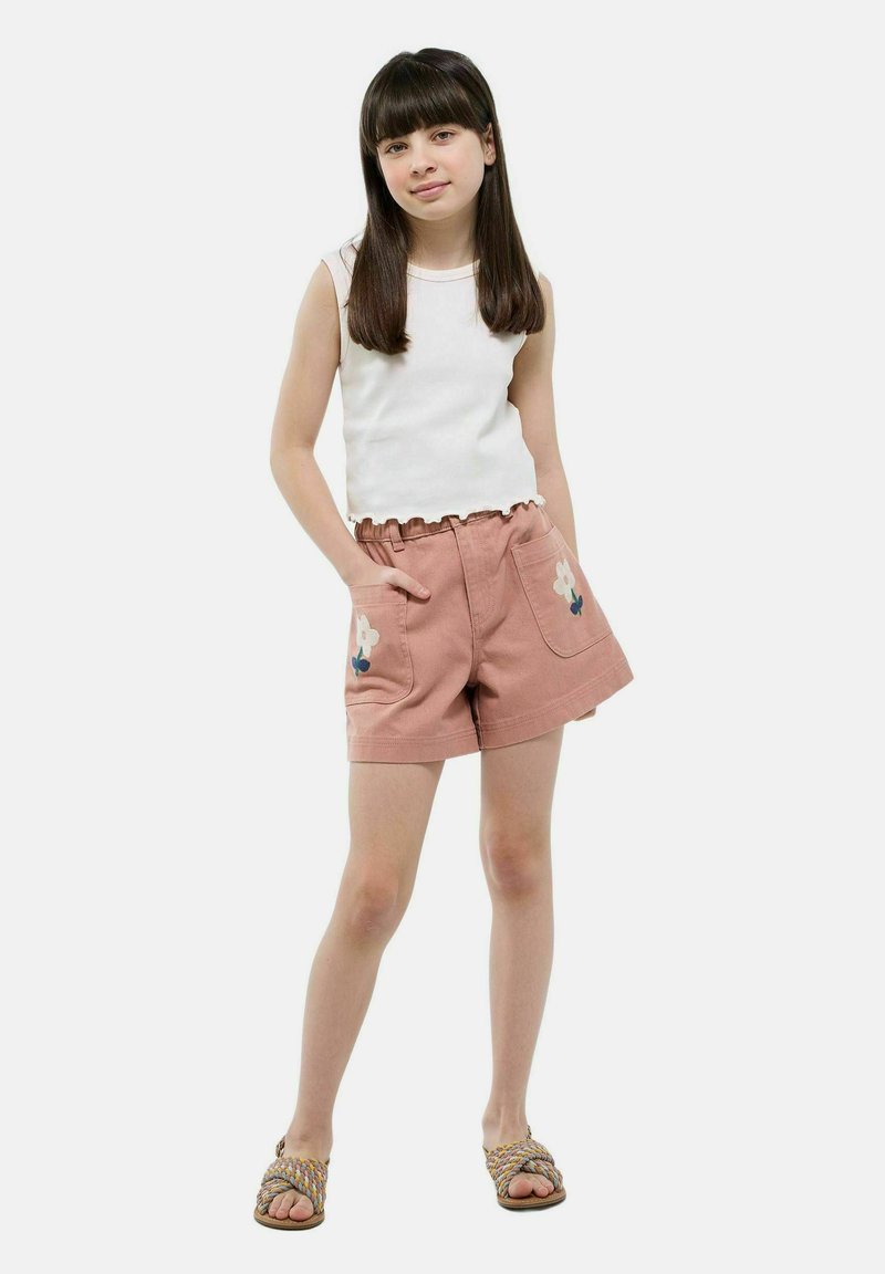 Un short rose clair avec une broderie florale sur les poches, associé à un débardeur blanc à côtes avec un ourlet festonné. Porté avec des sandales tressées.