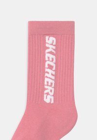 Rosa ribbad strumpa med en vit "SKECHERS"-logotyp längs sidan, tillverkad av mjukt material och med en standardform och textur för strumpor.