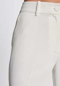 Pantaloni bianchi su misura con una texture liscia, vita piatta con chiusura a bottone e tasche laterali per una maggiore funzionalità.