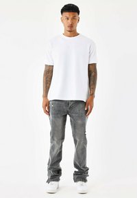 Camiseta blanca de manga corta con logo, combinada con jeans grises desgastados con bolsillos y zapatillas blancas. Textura de tela suave en general.