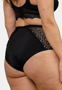 Culottes noires à taille haute avec un devant lisse et des détails en dentelle sur les côtés, dotées d'un tissu doux et d'un motif en dentelle complexe.