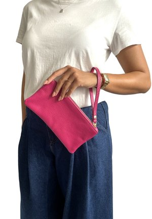 Clutch in pelle texturizzata rosa con chiusura a zip e tracolla coordinata, tenuto da una persona che indossa una maglietta bianca e pantaloni di jeans.
